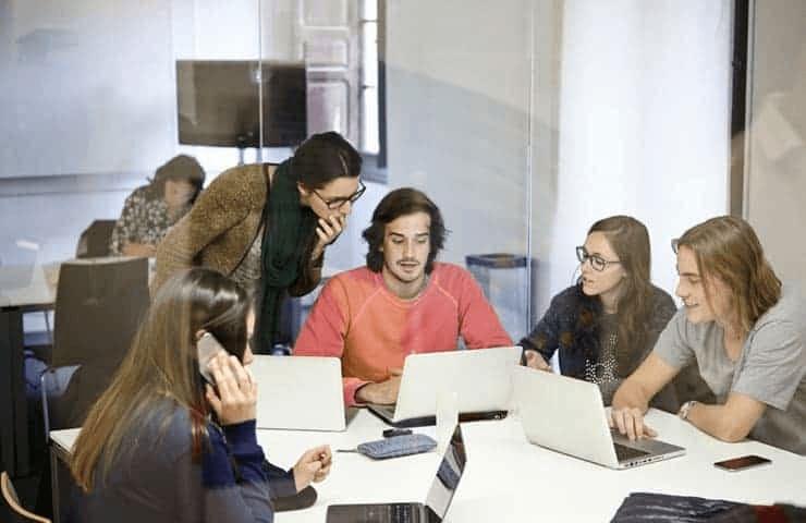 A group of young adults is engaged in discussion while using laptops at a modern office.