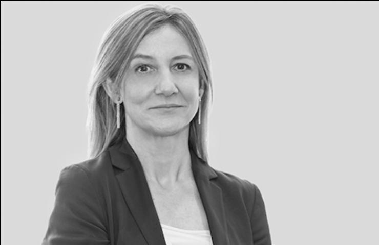 A black and white portrait of a woman with long hair, wearing a blazer over a blouse, posing with a slight smile.