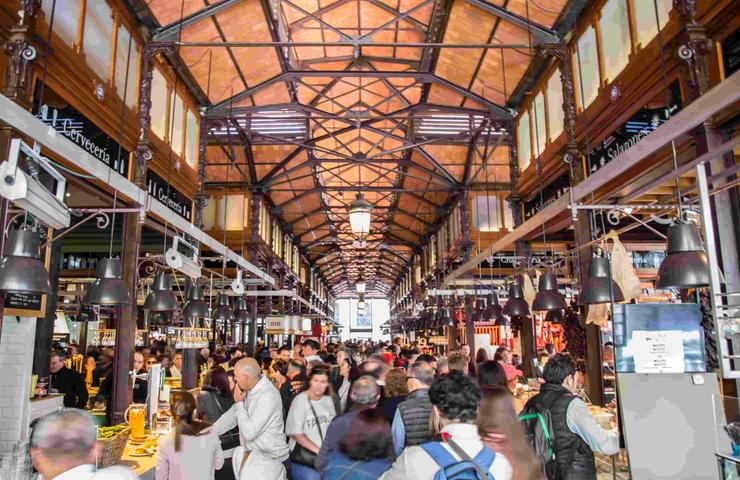 A bustling market hall filled with people and various food stalls.