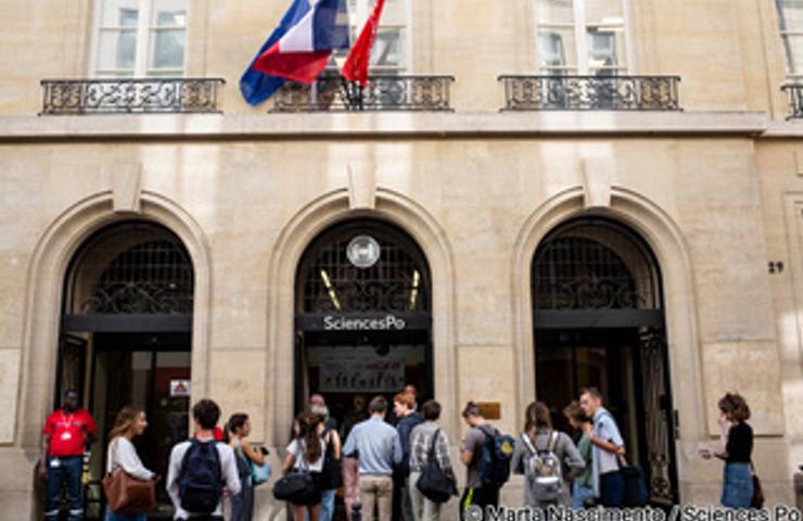 Students gather outside the entrance of Sciences Po, a prominent university in France, flanked by the French flag.