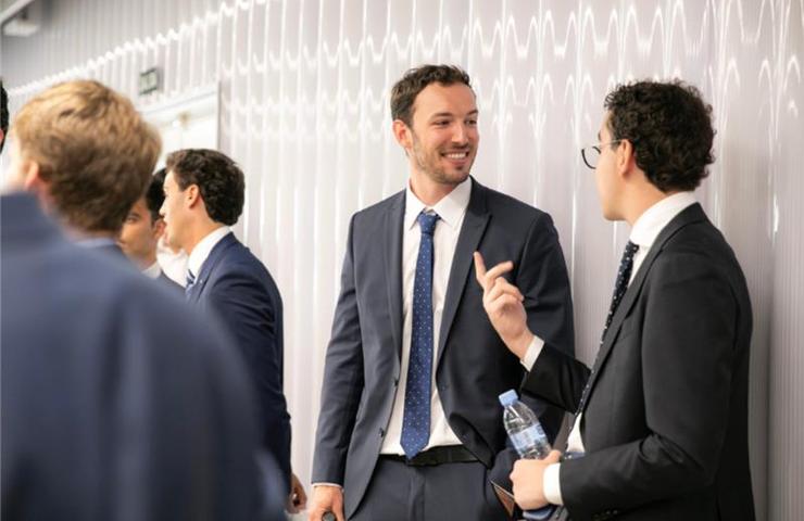 A group of men in suits are engaged in conversation at a professional event.