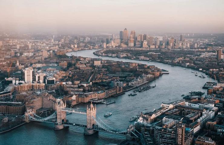 Aerial view of London showing the River Thames, Tower Bridge, and skyscrapers in the financial district during sunset.