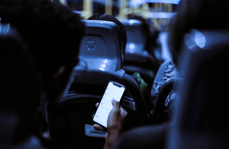 A person using a smartphone on a bus at night, with other passengers visible in the background.