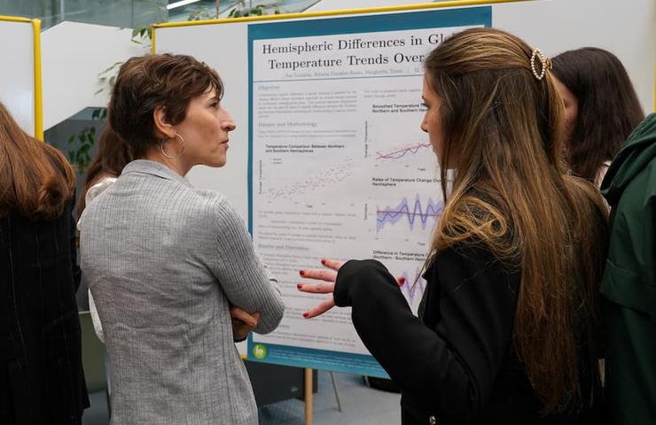 Two women are discussing in front of a research poster about hemispheric differences in global temperature trends.