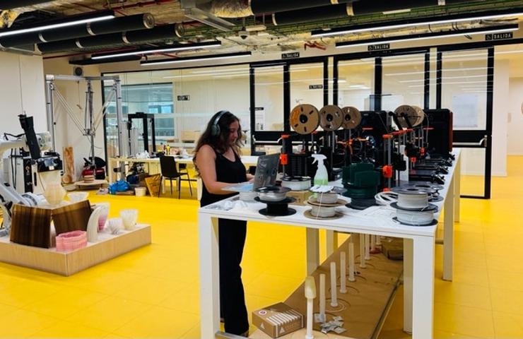 A woman is working at a table in a bright yellow workspace filled with various tools and materials.