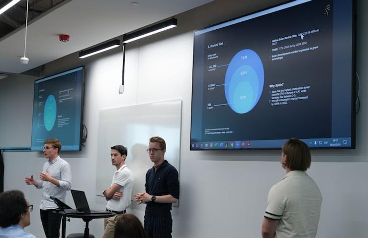 A group of people presenting a digital presentation in a modern classroom setting.