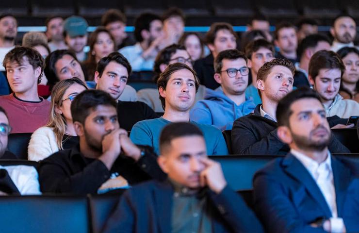 A diverse group of people sitting in a conference or lecture hall, attentively watching a presentation.
