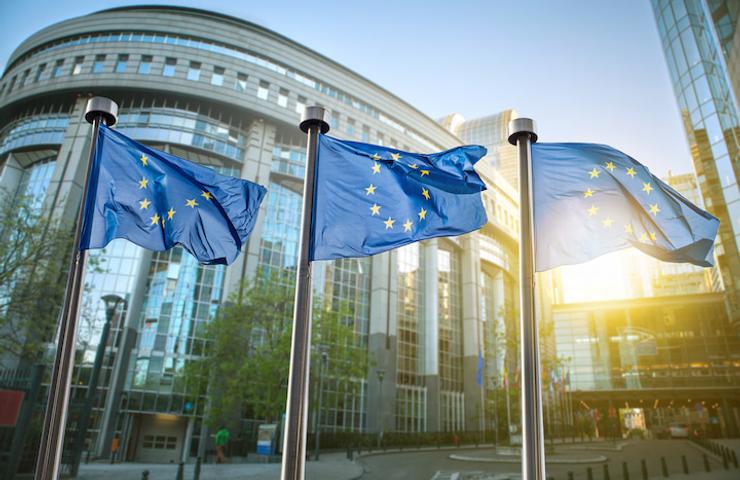 European Union flags flutter in front of a modern glass building.