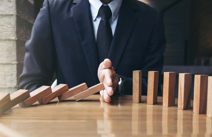 A person in a business suit stopping a line of falling dominoes on a wooden table.