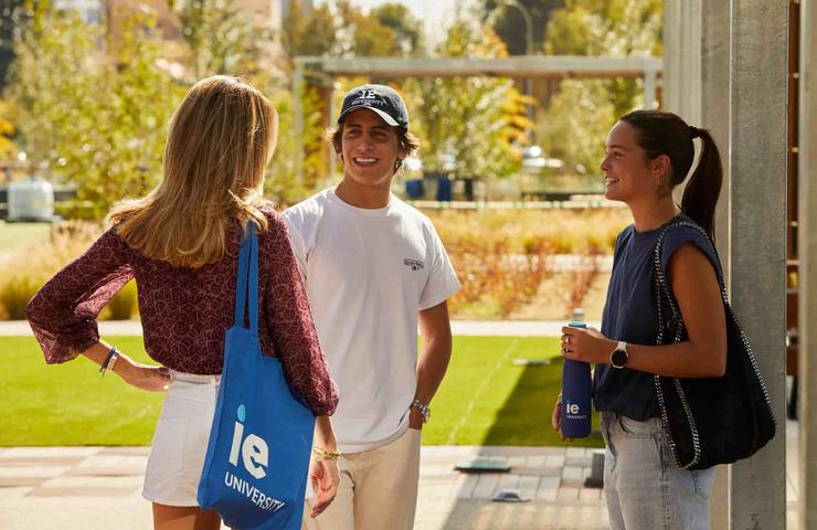 A group of three students engaging in conversation outdoors on a sunny day.