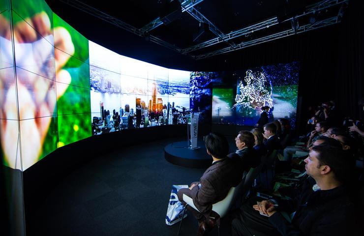 A large, modern presentation space with an immersive screen displaying various visuals and an audience seated in front.