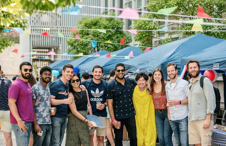 A group of friends posing together at an outdoor event with colorful decorations.