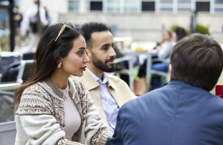 A group of three people sitting at an outdoor table, engaged in conversation.