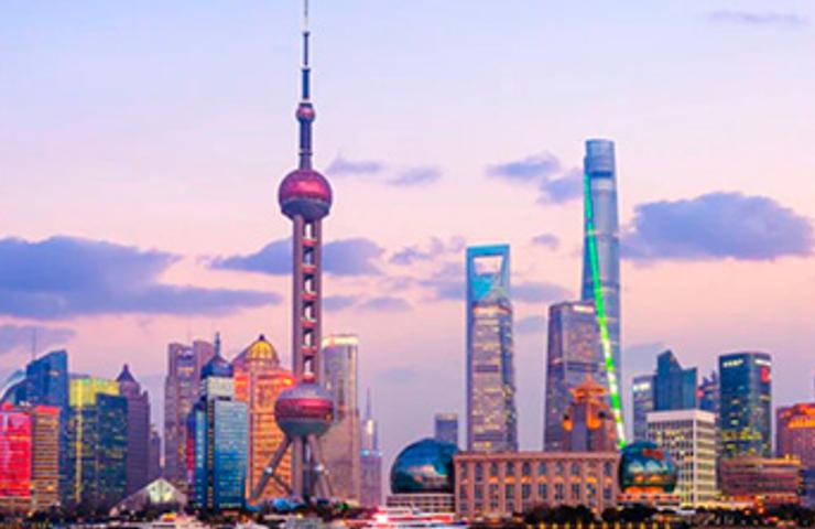 A panoramic view of the Shanghai skyline at dusk, featuring the Oriental Pearl Tower and illuminated skyscrapers.