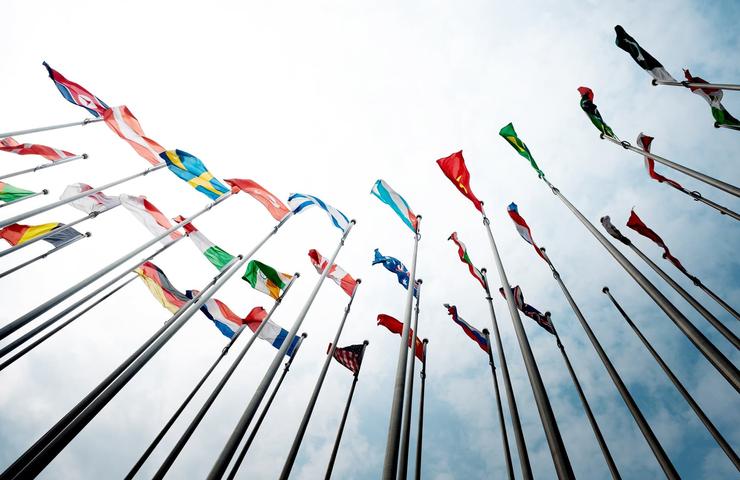 Colorful international flags fluttering against a bright sky, viewed from a low angle.