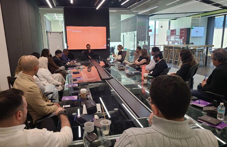 A group meeting is taking place in a modern conference room with several attendees seated around a long table.