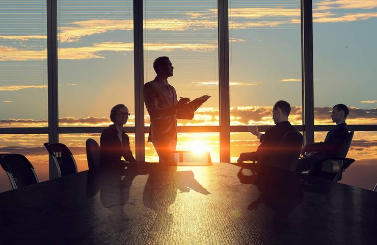 A group of business professionals in a meeting at sunset with a city skyline in the background