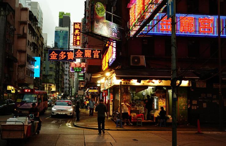 A bustling street in Hong Kong illuminated by neon signs at dusk.