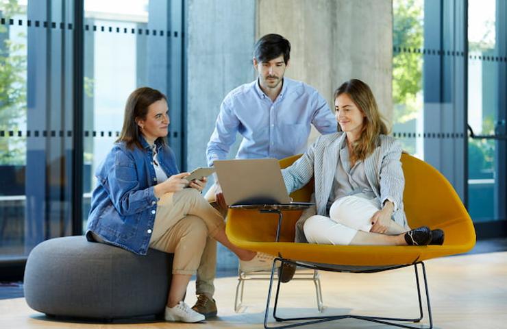 Three professionals, two women and one man, discussing over a laptop in a modern office setting