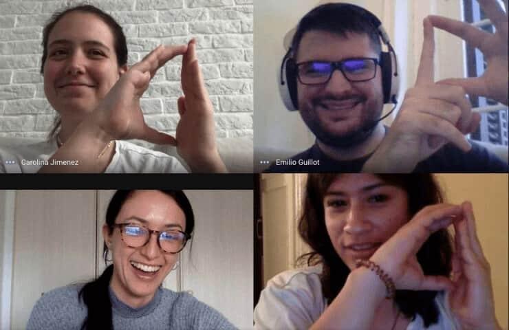 Four people smiling on a video call, making heart shapes with their hands.