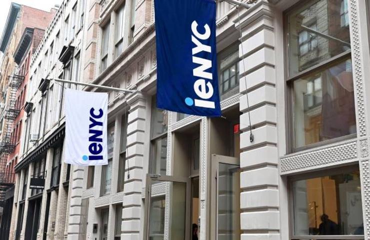 A view of a city street with large blue flags displaying 'ieNYC' hanging from a modern building facade.