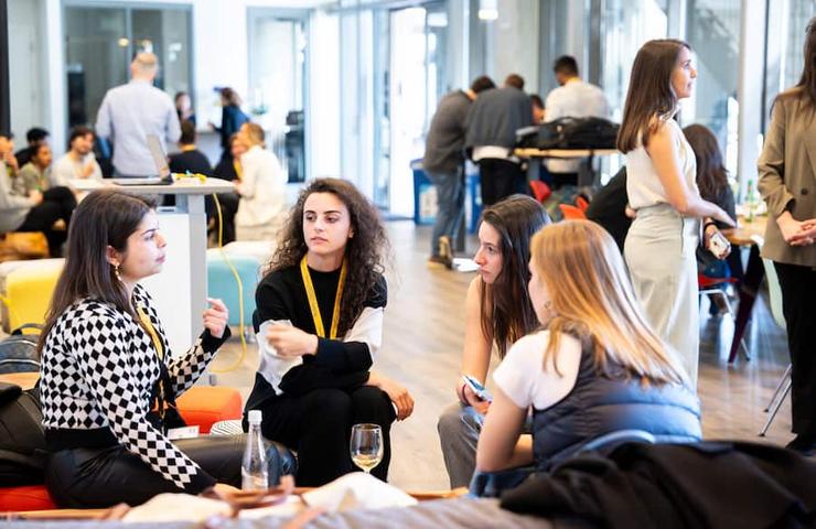 A group of women engaged in a conversation at a networking event inside a modern office space.