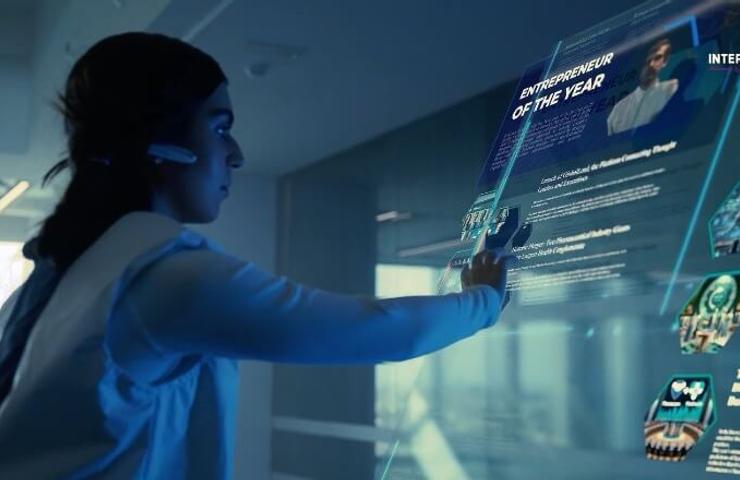 A woman interacts with a futuristic holographic display showing various awards and digital information.