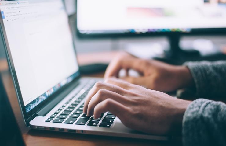 Person typing on a laptop with another monitor in the background.