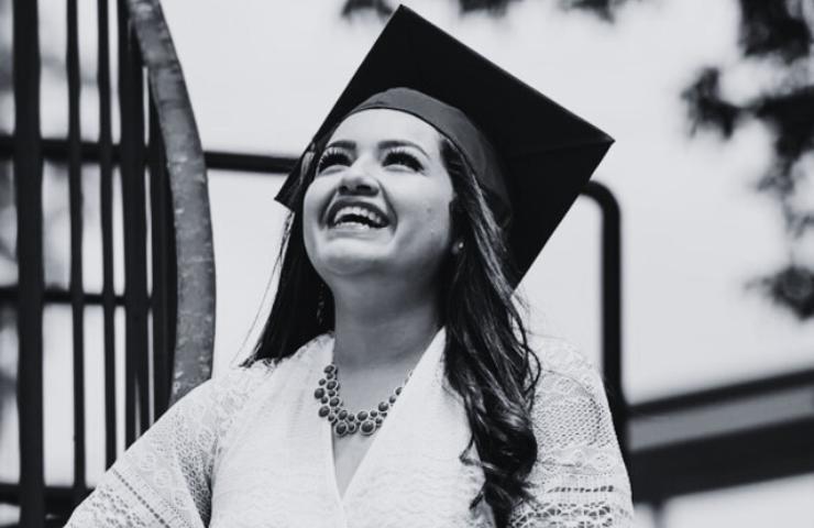 A joyful graduate woman in a cap and gown laughing outdoors.