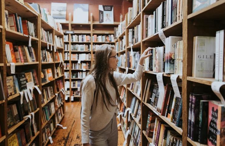 A young woman browsing books in a cozy bookstore aisle.