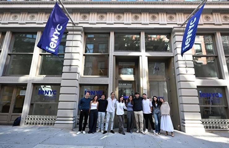 A group of people stands together in front of a modern building with flags that read 'enYC'.