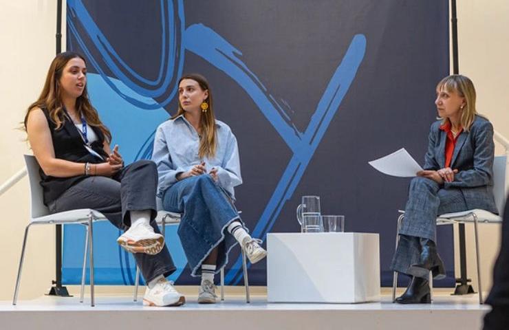 A panel discussion featuring three women seating on chairs with a modern backdrop.