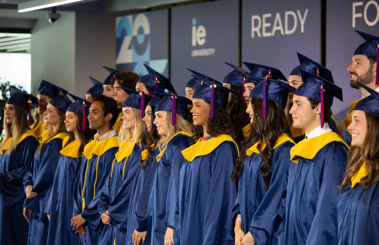 A group of graduates in blue gowns and yellow stoles stand together in a ceremony.
