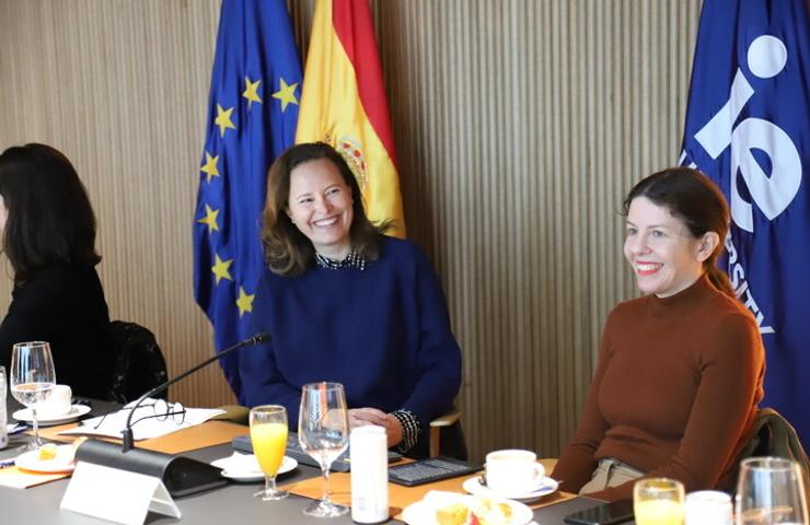 A group of women sitting at a table during a meeting, smiling and engaging in conversation.