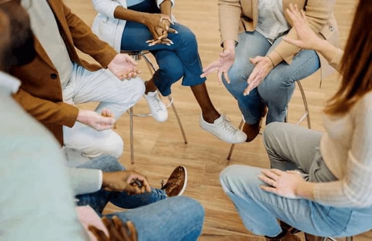 A group of people sitting in a circle, gesturing with their hands during a discussion or activity.