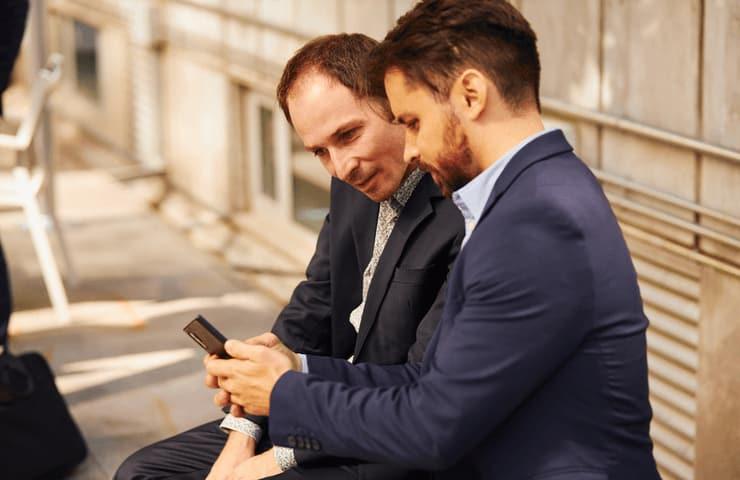 Two men in business suits sitting together and looking at a smartphone.