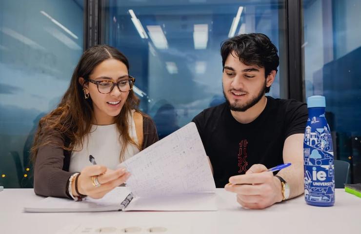 Two students are collaborating while studying at a table in a modern classroom.