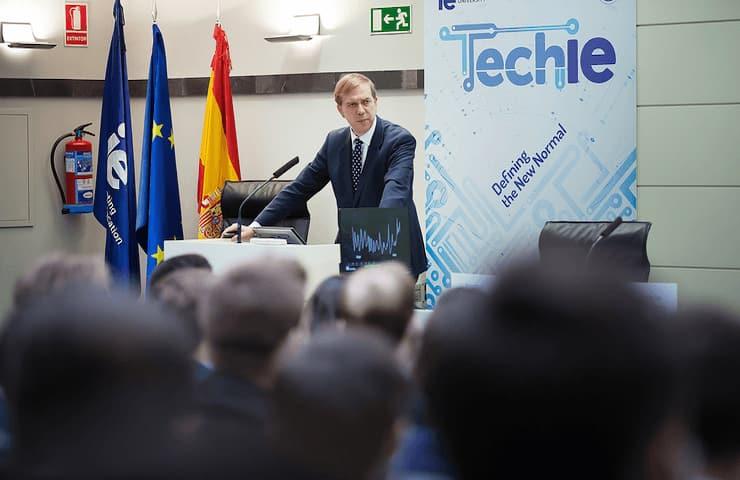 A man giving a speech at a podium with 'Techie' and EU and Spanish flags in the background.