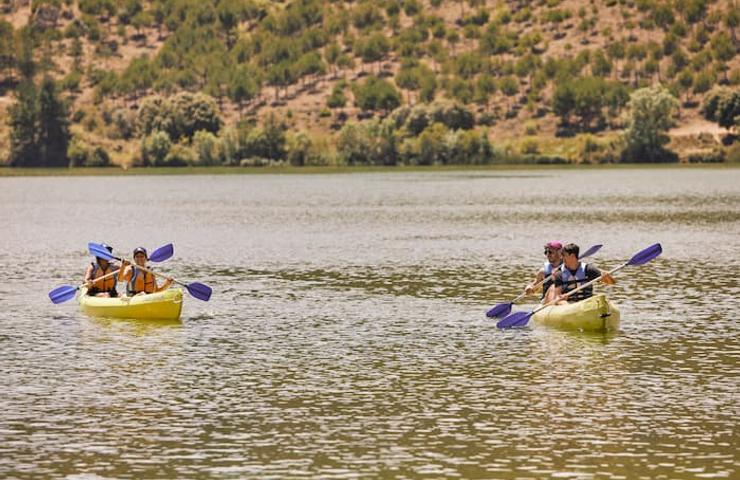 Two kayaks, each with two people, are paddling on a calm lake surrounded by hills.