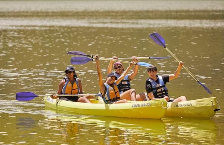 Three people joyfully kayaking on a calm river, waving and smiling.