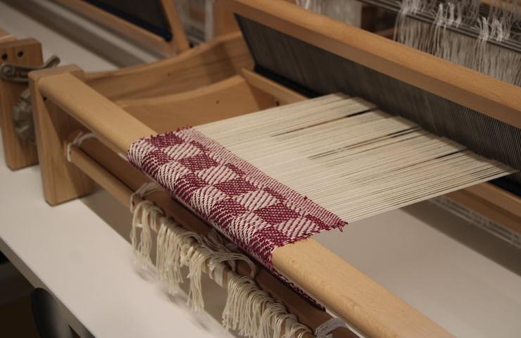 A close-up view of a loom with partially woven fabric in a checkered pattern.