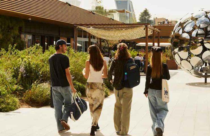 Four people walking through a sunny outdoor plaza with contemporary sculptures and landscaping.