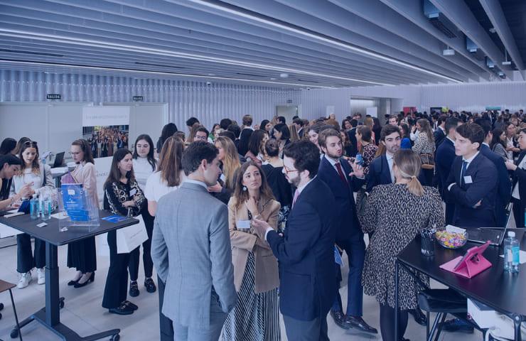 A bustling indoor networking event with numerous people engaging in conversations around booths.