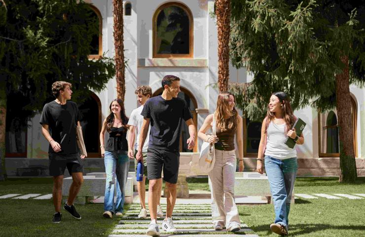 A group of young people walking together in a park-like setting with trees and a building in the background.