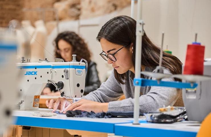 A young woman focused on sewing at a machine in a creative workspace.