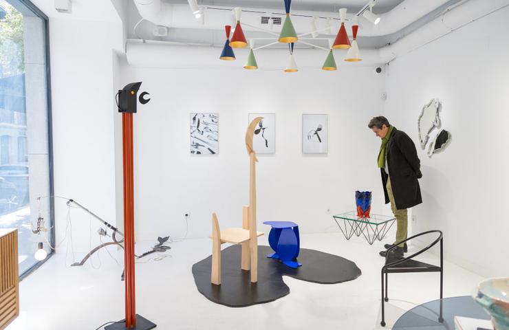 A person browsing an art exhibition with various contemporary sculptures and wall art pieces in a white gallery space.