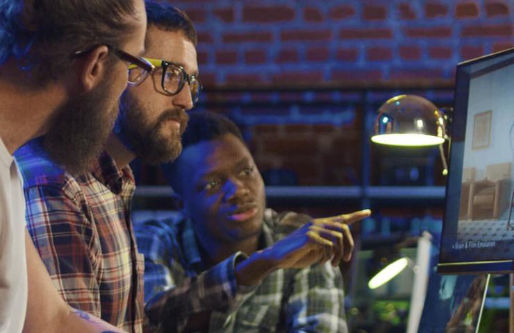 Three men collaborating at a computer workstation in a modern office setting.