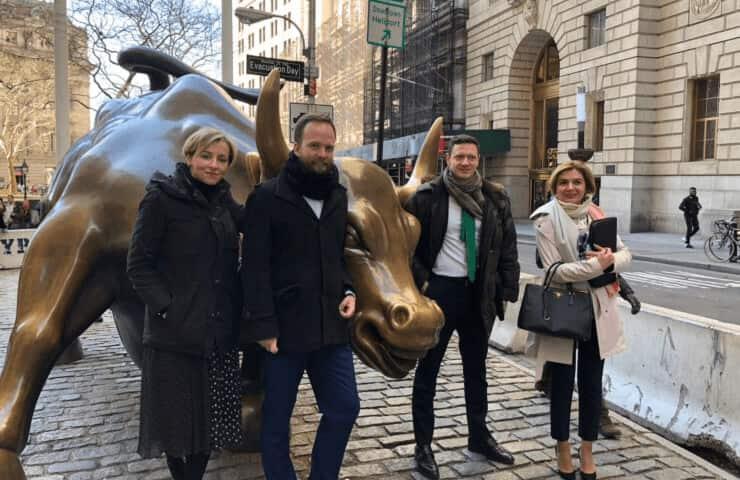 Four people posing next to the Charging Bull sculpture in a city setting.