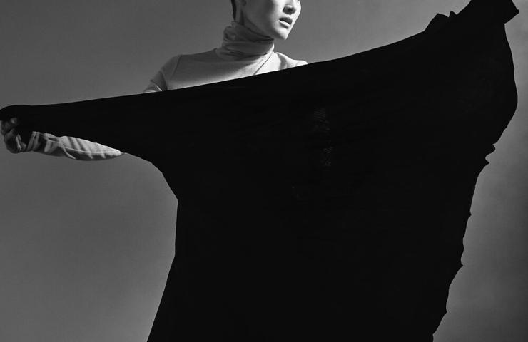 A black and white photo of a woman in a dynamic pose with a flowing black garment.