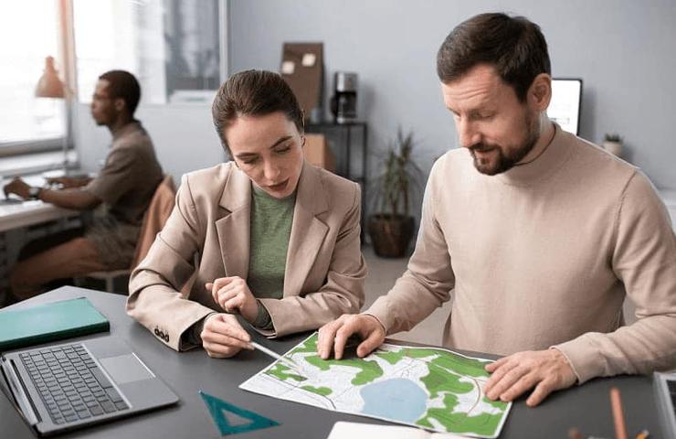 Two professionals, a man and a woman, are examining a map together on a desk in an office environment.